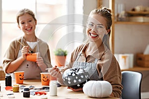 Smiling mother and daughter sitting at wooden table and making Halloween decor together at home