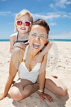 Smiling mother and daughter in swimsuits at sandy beach