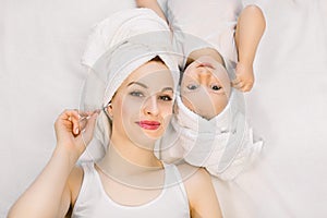 Smiling mother and daughter in towels at bathtime. Young Caucasian woman mom with her little girl toddler, lying