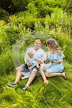 Smiling mother and father with little baby girl enjoy picnic in summer