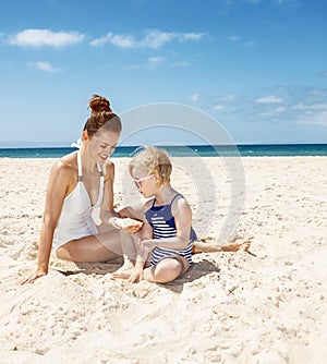 Smiling mother and girl in swimsuits at sandy beach playing