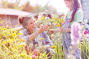 Smiling mother giving flowers to daughter while gardening at farm