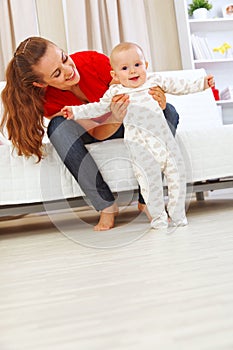 Smiling mother helping cheerful baby learn to walk