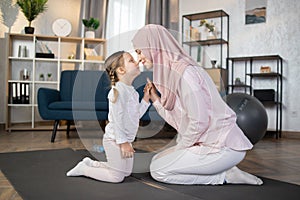 Smiling mother and her adorable little daughter relaxing after sports sitting on the mat