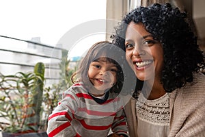 Smiling mother and her cute daughter sitting together at home