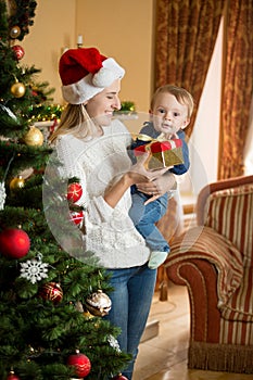 Smiling mother holding her baby boy at Christmas tree and giving