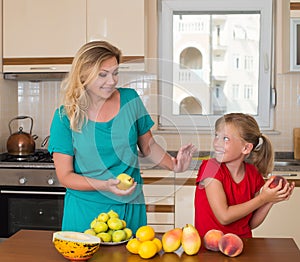 Smiling mother with keeping sweet pear daughter. Healthy eating - woman and child in the kitchen with different kinds of fruits