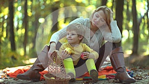 Smiling mother with kid having fun in autumn park. Mother and son having fun outdoor. Happy family with male children