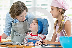 Smiling mother and kids interacting with each other while preparing cookies