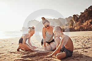 Smiling Mother and kids playing in the sand at the beach