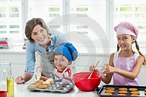 Smiling mother and kids preparing cookies in kitchen