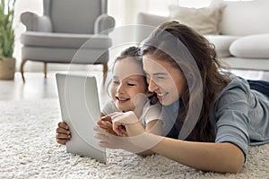 Smiling mother lie on floor with daughter use digital tablet