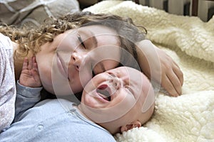 A smiling mother lies on the bed near her crying baby