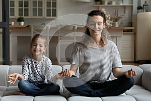 Smiling mother and little daughter meditating on couch together