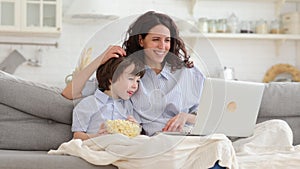 Smiling mother and little preschool son watch funny video, cartoon on laptop together in living room