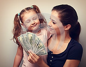 Smiling mother looking on happy daughter holding cash of dollars