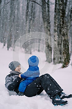 Smiling mother lying on her back in the snow with a small child sitting on her stomach