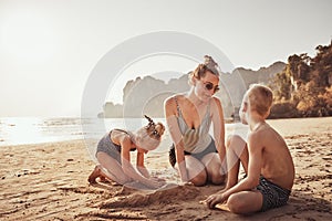Smiling Mother playing with her children on a sandy beach