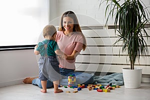 Smiling mother playing with her cute toddler son at home