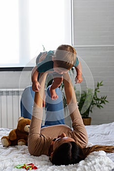 Smiling mother playing with her cute toddler son at home in the bed. Using plush bear and baby toys. Maternity concept