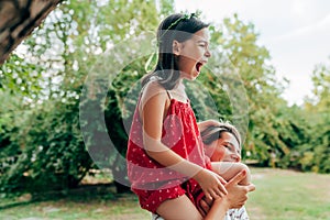 Smiling mother playing and riding on her shoulder her daughter in the park. Happy kid having fun with her mom enjoying the time