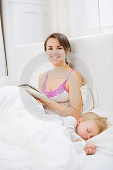 Smiling mother reading book while baby sleeping