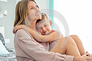 Smiling mother sitting on bed with her child, hugging, spending morning time together