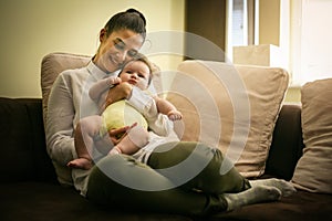 Smiling mother sitting on couch and holding baby girl in arms.