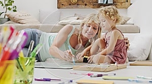 Smiling mother smiles at curly haired blonde daughter child, preschool learning activity at home, concept of healthy growing,