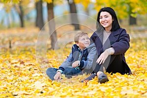 Smiling mother and son sitting in fall leaves.