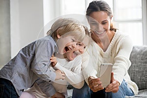 Smiling mother taking selfie with two cute kids on smartphone