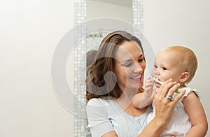 Smiling mother teaching cute baby how to brush teeth with toothbrush