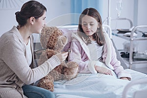 Smiling mother and weak daughter taking care of teddy bear in th