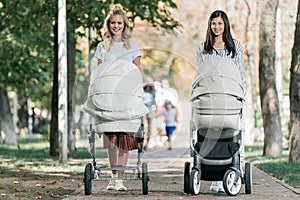smiling mothers walking with baby strollers in park and looking
