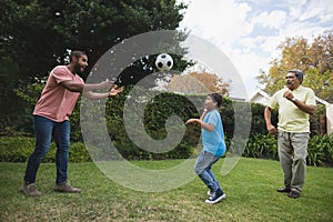 Smiling multi-generation family playing with soccer ball at park