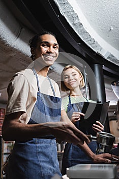 Smiling multiethnic baristas in aprons holding