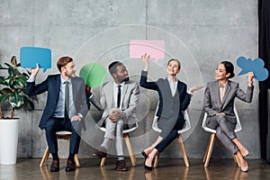 Smiling multiethnic businesspeople holding speech bubbles and thought bubble while sitting in