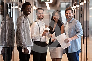 Smiling multiethnic colleagues posing for picture in office hallway