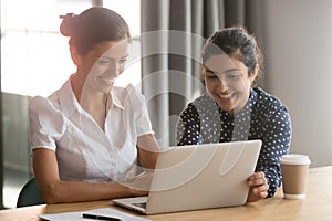 Smiling multiethnic female employees laugh working together on laptop