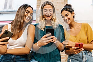 Smiling multiethnic female friends having fun together using mobile phone