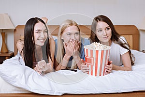 smiling multiethnic girls lying on bed with popcorn