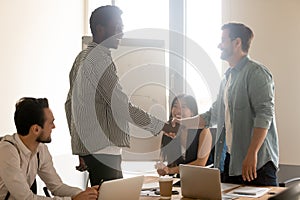 Smiling multiethnic male employees handshake at briefing