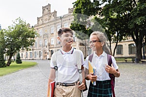 Smiling multiethnic schoolkids with notebooks walking