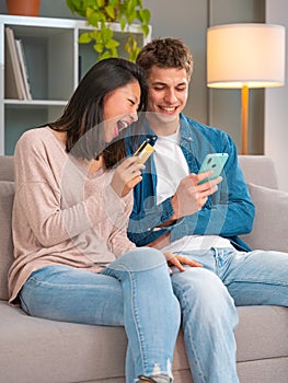 Smiling multiethnic young couple shopping online with credit card and smartphone inside.Vertical