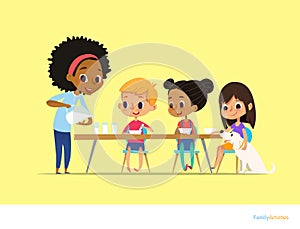 Smiling multiracial children sit at table and have breakfast while mother pour milk into gasses. Kids eating healthy morning meal.