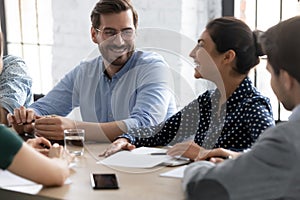 Smiling multiracial colleagues laugh discussing ideas at meeting