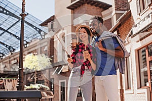 Smiling multiracial couple taking selfie on smartphone using selfiestick in the city at daytime