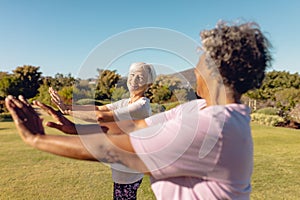 Smiling multiracial female seniors stretching hands against clear sky in yard at retirement home