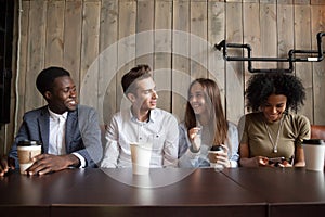 Smiling multiracial friends drinking coffee having fun in cafe