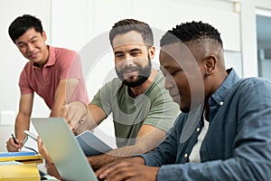 Smiling multiracial male coworkers looking at businessman working over laptop in office